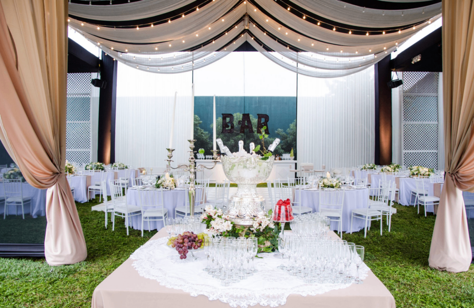 Elegant tent interior with tan drapes, string lights and a champagne bar