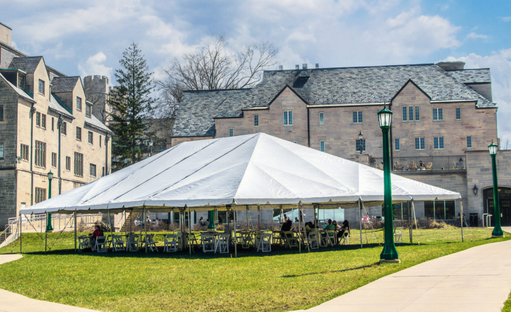 Large white frame tent set up outside a stone estate under blue sky