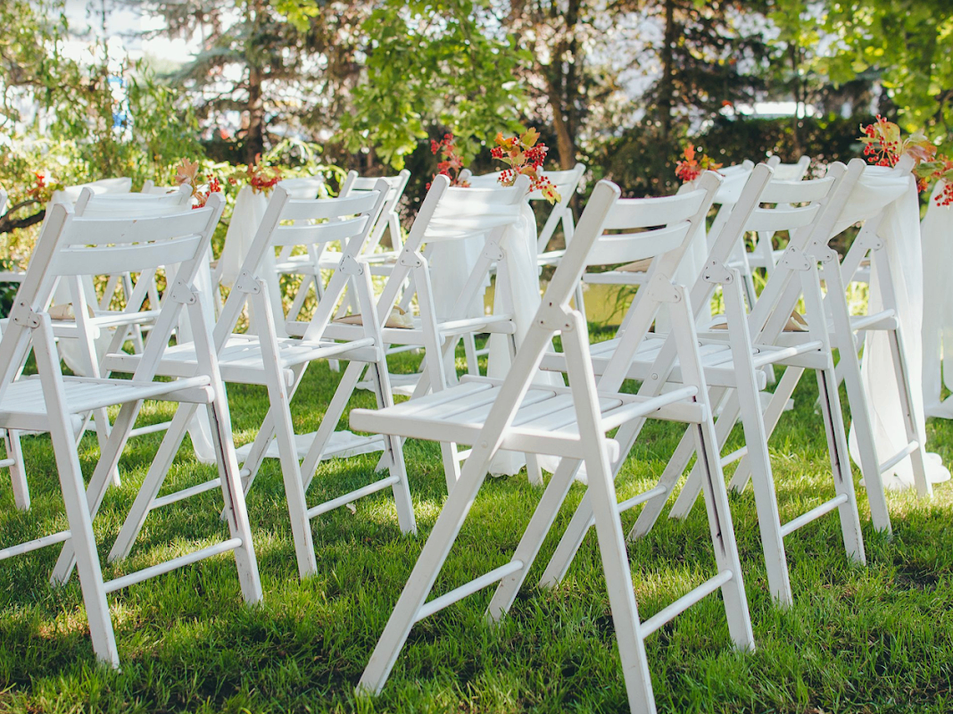 Rows of white folding ceremony chairs decorated with fall florals on the grass